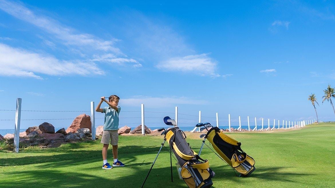 A boy standing on a golf course with a golf bag